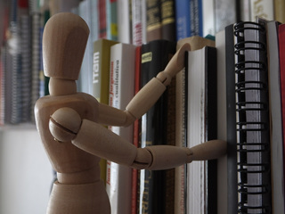 A wooden figure appears to be browsing for books in a library.